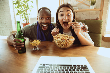 Excited football fans watching sport match at home, remote support of favourite team during...