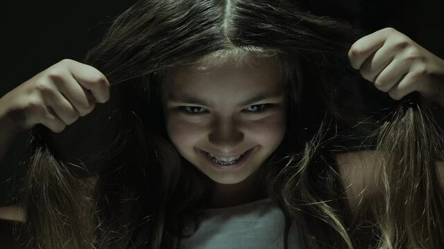 Portrait of a scary girl with gaze holding long hair with her hands in a dark room with flickering light
