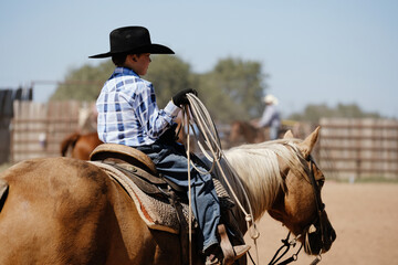 Young cowboy in western cowboy hat for ranch lifestyle horseback riding palomino with rope.