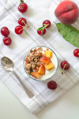 Breakfast parfait with yogurt, granola, peach and sour cherries in a glass. Vintage silver spoon and fruit in the background