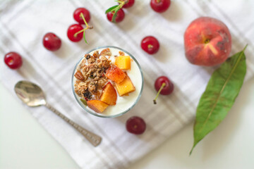 Fototapeta na wymiar Breakfast parfait with yogurt, granola, peach and sour cherries in a glass. Vintage silver spoon and fruit in the background
