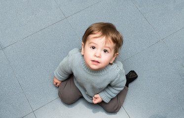 A one-year-old baby kneeling on the kitchen floor, looking at me