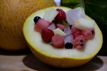 Summer fruit salad in the melon. Colored berries inside yellow. On a wooden background. Yummy and healthy eating.