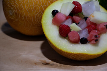 Summer fruit salad in the melon. Colored berries inside yellow. On a wooden background. Yummy and healthy eating.