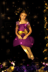 Christmas girl sitting in dark like Merry Christmas tree. Beautiful New Year magic lights. Holiday Hairstyle and fairy dress. Beauty Fashion Model in full length. Magic lights. Gold and purple color