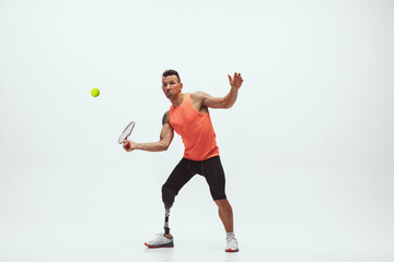 Athlete with disabilities or amputee isolated on white studio background. Professional male tennis player with leg prosthesis training in studio. Disabled sport and healthy lifestyle concept.