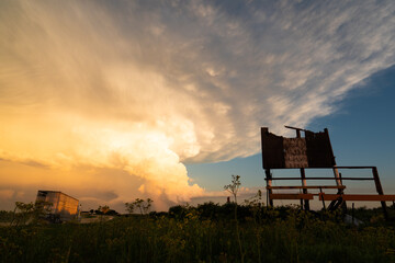 A truck driving into supercell storm at sunset, torn billboard after the storm.