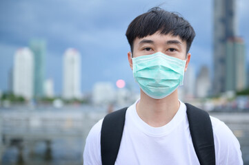 A young Asian tourist man is wearing protective mask standing outside , Coronavirus protection, new normal travel concept