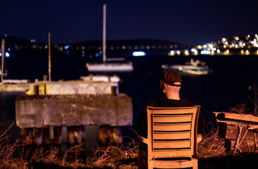A single man, sitting on a chair outdoor, thinking and watching the view at nighttime