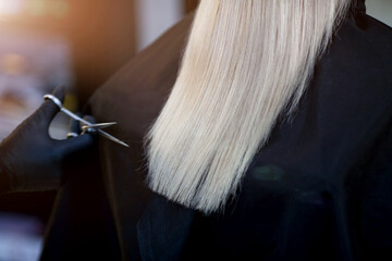 A hairdresser in rubber gloves holds a pair of scissors and a comb. Woman getting a new haircut.