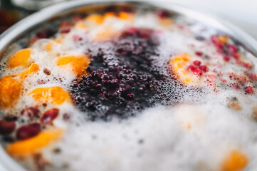 Fresh fruits are boiled in boiling water in a metal pan on a stove with bubbles and foam close-up. Cooking a delicious compote of apricot, apples, cherries, raspberries. Photography, concept.