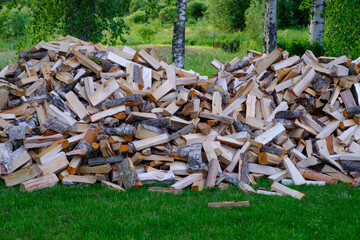 A large pile of firewood on the meadow. Trees/timber has been cut and split into firewood to be used as fuel for heating in fireplaces and furnaces in the.