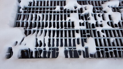 Close-up of white pieces of snow on a metal grate. Snow falls through the grating, revealing voids. Abstraction of snow and metal lattice. On a winter day, outdoors in the evening. Texture.