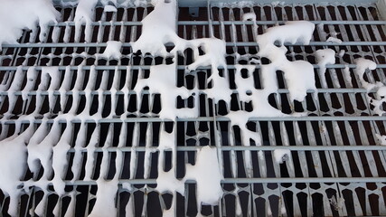 Close-up of white pieces of snow on a metal grate. Snow falls through the grating, revealing voids. Abstraction of snow and metal lattice. On a winter day, outdoors in the evening. Texture.