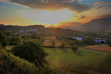 Obraz premium a view of the hills and fields in Buccino, Italy during a colorful sunset.