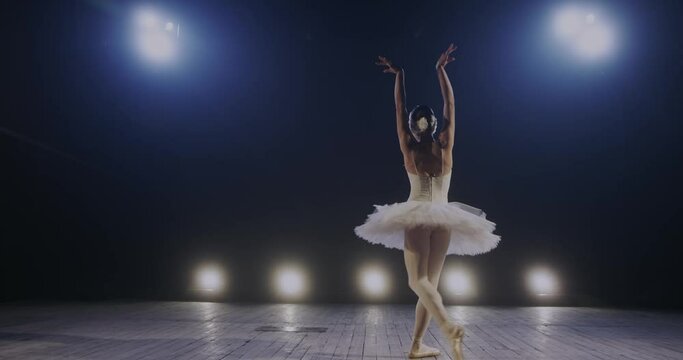 Rear of slim woman working on stage in white tutu while dancing gently moves of classical ballet in theater perfomance. Back view on young ballerina dance.