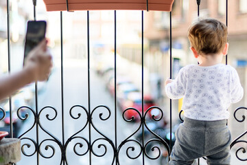 A year and a half old boy playing on the balcony and watching the cars go by in the quarantine