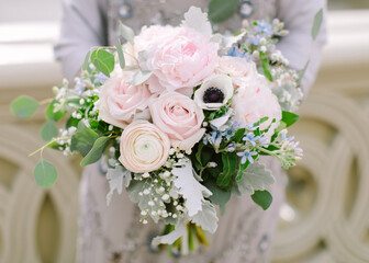 Beautiful bridal bouquet made of creamy and light pink peonies, roses, ranunculuses, baby breath and eucalyptus branches
