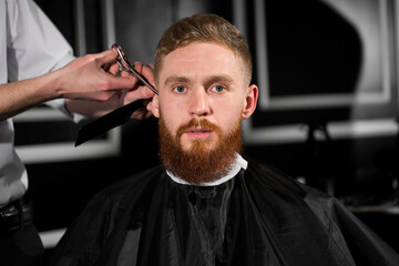 Master cuts hair and beard in the Barber shop. Hairdresser makes hairstyle using scissors and a metal comb