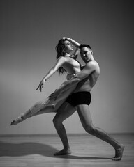 A man and a woman are dancing modern ballet. Acrobatic couple perform number on a white background. A duet of gymnasts rehearsing a performance with support. Monochrome photo.