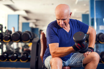 A portrait of senior man in the gym training with dumbbells. People, health and lifestyle concept