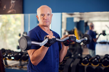 A portrait of senior man in the gym training with barbell. People, health and lifestyle concept