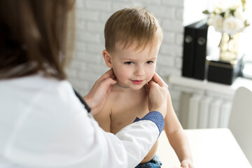 Pediatrician examining thyroid gland of little boy in clinic