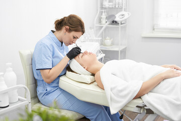 Obraz premium Doctor cosmetologist makes a multi-stage facial cleansing procedure to a young attractive woman in a beauty salon. Summer skin care