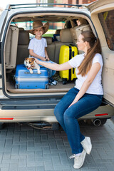 European woman with son and puppy Jack Russell travel by car. kid and his mother and a small dog are sitting in the trunk and heading out for summer vacation. Independent family trip with children.