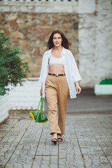 Young happy beautiful girl is walking in a shirt and pants with a bouquet of flowers of sunflowers on a city street