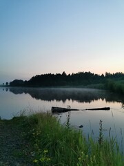 Foggy dawn on river. Landscape with forest, sky, grass and reflection in water