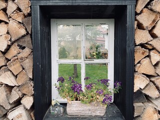 Altes Holzfenster mit Blumen geschmückt, umringt von gespaltenen Holzscheide