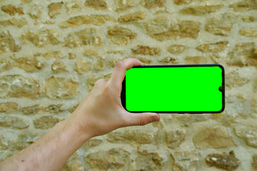 man hand holding a phone horizontally in front of an old stone wall.