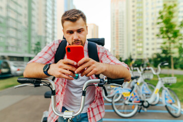 Man is sitting on a bicycle and uses a smartphone with a focused face. Focus on the smartphone. Man shares a bicycle through a mobile application