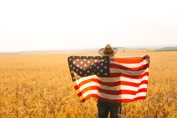 Young caucasian farmer energetically raised the US flag in a picturesque field of wheat.