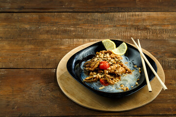 plate with funchose and chicken with vegetables in pad Thai sauce next to chopsticks on a stand.