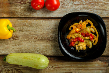 Vegetable stew stew on a black plate and a number of vegetables on a wooden table.