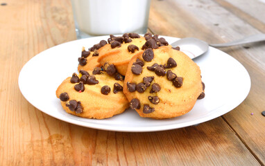 Freshly baked chocolate chip cookies in plate and milk on wooden board