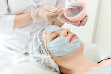 Fototapeta na wymiar Cosmetologist in gloves apply mask to face of girl in beauty salon.