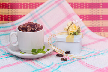 Beautiful gift with bow and coffee grains in mug, on a nice napkin