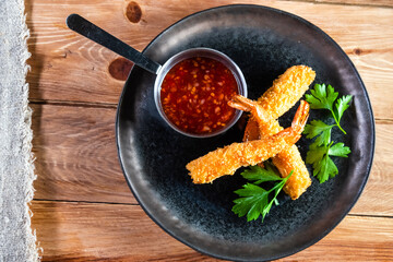 Appetizing fried shrimp on a dark plate stand on a wooden table with sauce and herbs. The concept of food, serving, bars and restaurants