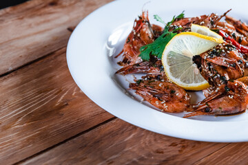 Appetizing fried shrimp with specialties, sesame seeds and lemon, on a white plate on a background of wood. Food concept in restaurants and bars
