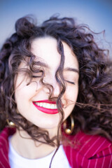 Beautiful brunette girl with curly hair, in a red strict suit, business clothes, lady, red lipstick on her lips