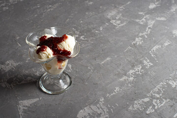 White balls of vanilla ice cream with raspberry jam in a dessert glass. Decorated ice cream on a table made of dark, rough concrete. Copyspace.