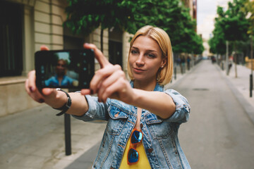 Naklejka premium Gorgeous young woman making self portrait with a cell phone camera while enjoying a day out strolling in new city at summer vacation, stylish female hipster taking a picture of herself on smart phone