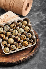 Quail eggs in a gray cardboard box. Close-up photo. Black concrete background. Healthy protein foods. Small speckled eggs for breakfast