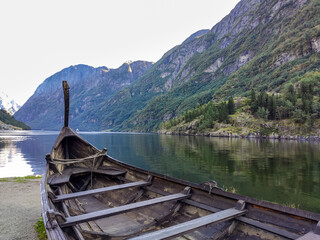 Fototapeta na wymiar Viking boat old wooden drakkar with dragon head close-up on coast of Naeroyfjord surrounded by mountains, Gudvangen, Norway