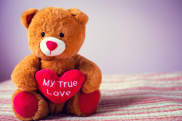Obraz premium A teddy bear with a heart in its paws sits on a bed against the background of the wall