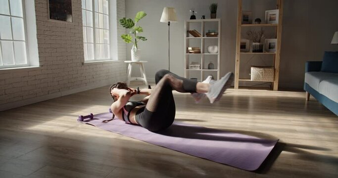Young determined female athlete doing crunches and listening to music. Motivated sportswoman has cross fit training at home - healthy way of life concept 4k footage