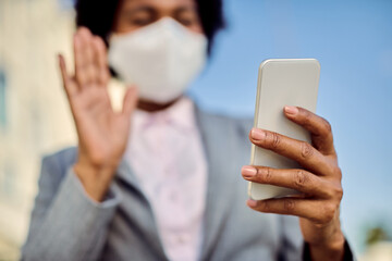 Close-up of black businesswoman with face mask using smart phone outdoors.